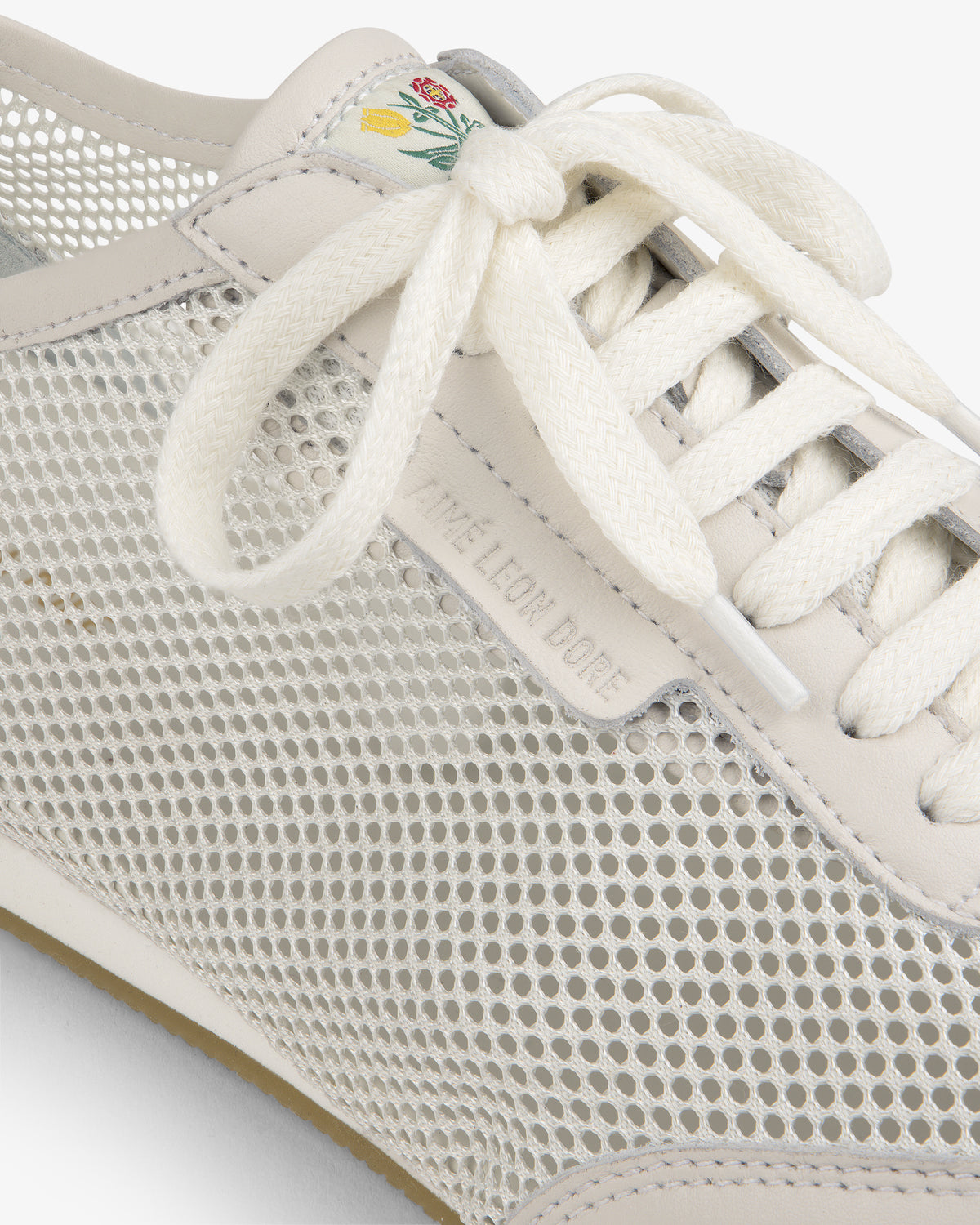 Close-up of the Low Profile Mesh Trainer featuring mesh sides, white laces, and a green-yellow floral tongue detail.