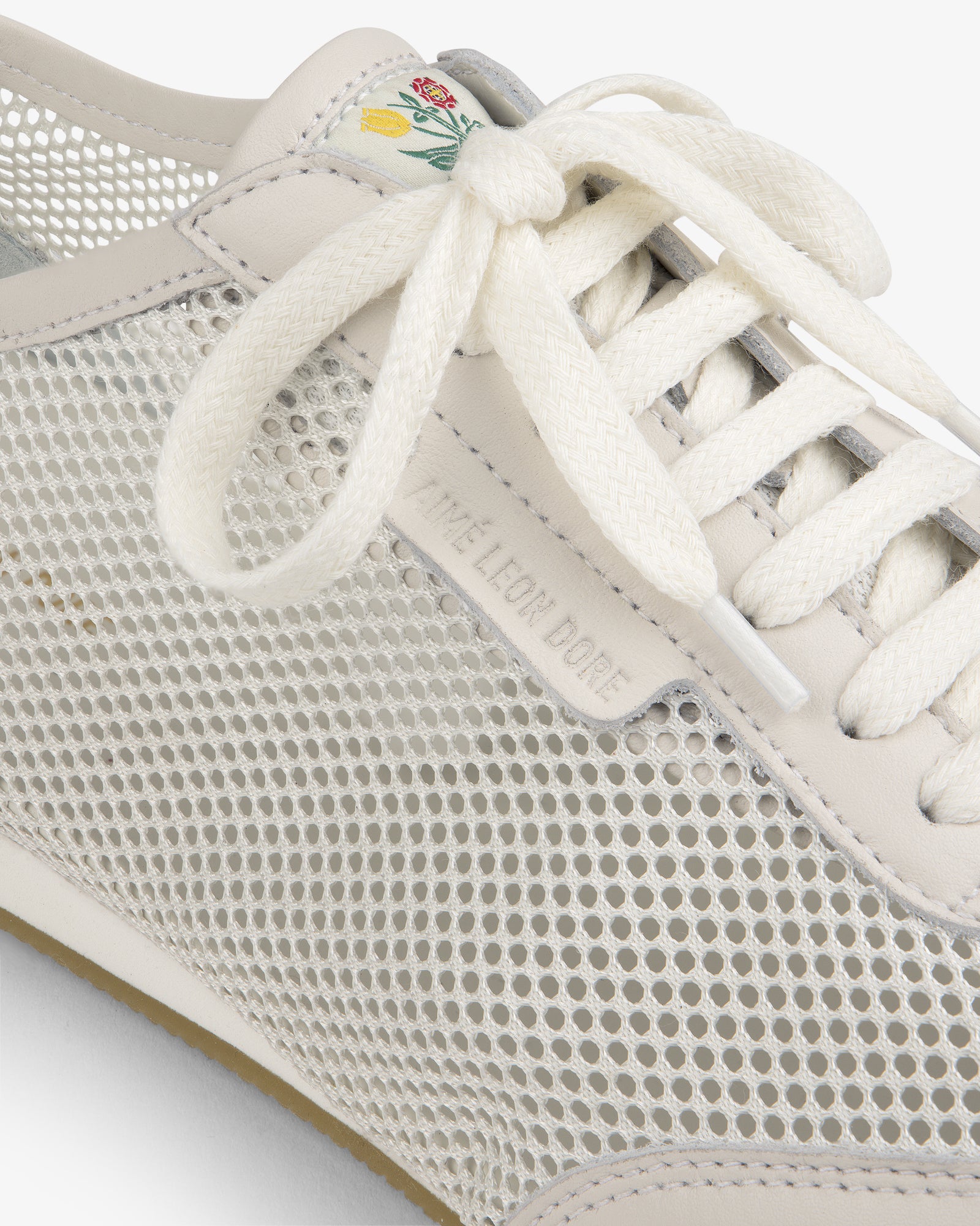 Close-up of the Low Profile Mesh Trainer featuring mesh sides, white laces, and a green-yellow floral tongue detail.