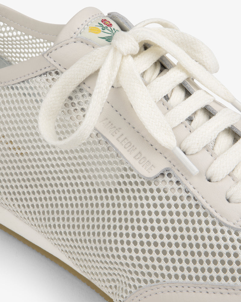 Close-up of the Low Profile Mesh Trainer featuring mesh sides, white laces, and a green-yellow floral tongue detail.