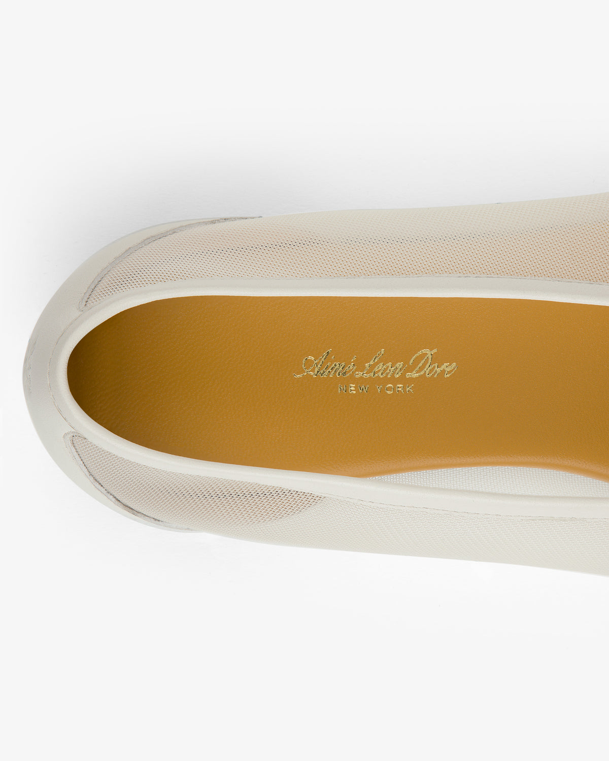 A close-up top view of the Mesh Ballet Flat, a white slip-on shoe with a tan insole and Aimé Leon Dore NEW YORK inside.
