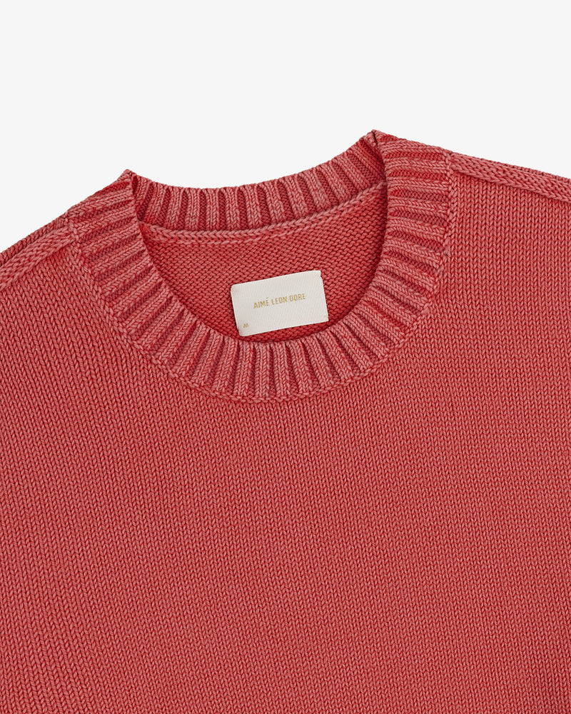 A close-up of the Washed Inside Out Sweater, a pink knitted crew neck with a visible label inside the collar.