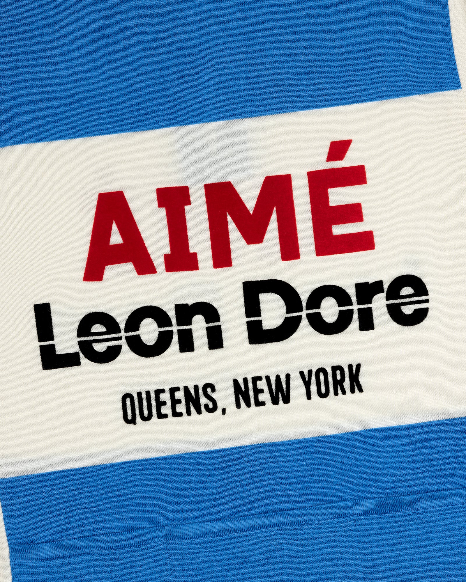 Close-up of a Merino Wool Cycling Jersey with AIMÉ Leon Dore QUEENS, NEW YORK on blue and white stripes.