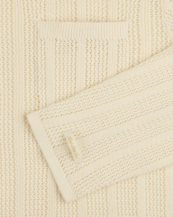 Close-up of the Racking Stitch Crewneck Sweater in cream with a small front pocket and a sleeve fabric label.