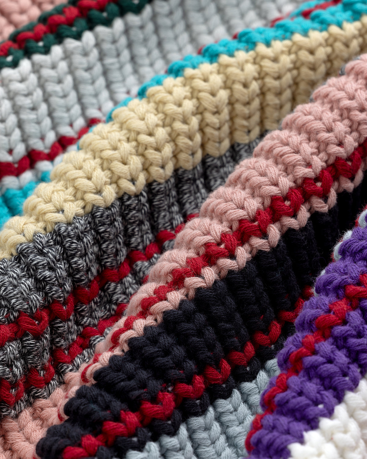 Close-up of the Striped Crewneck Sweater featuring rows of textured knits in beige, pink, grey, and blue yarns.