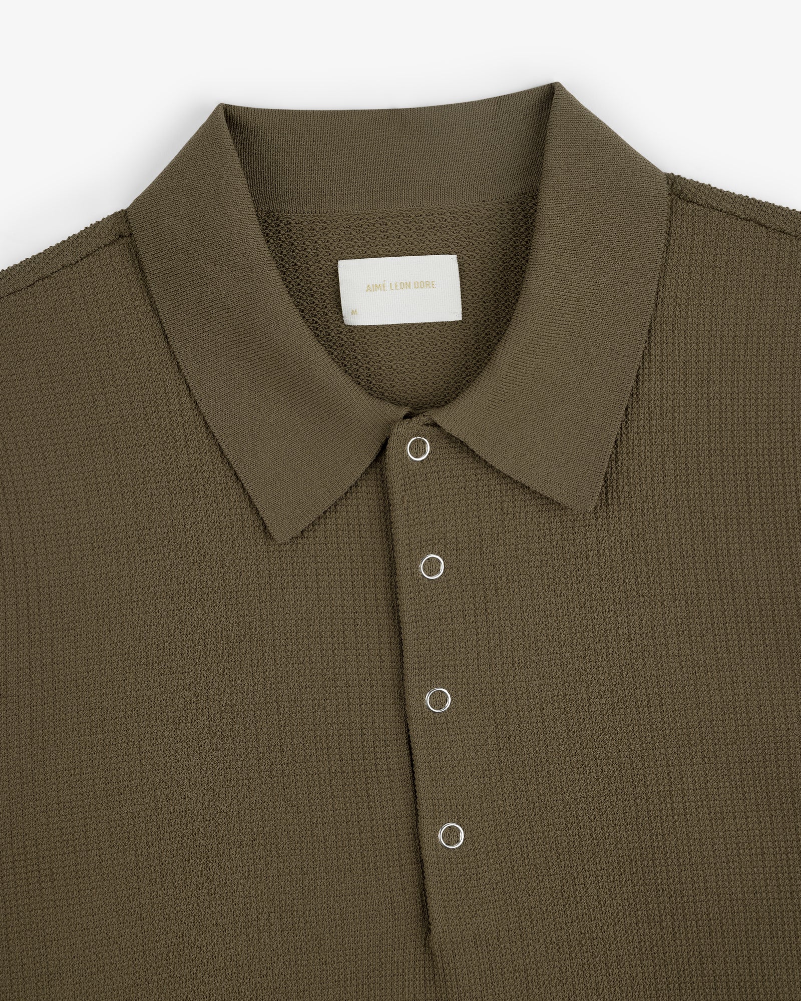 Olive green Knit Polo with textured fabric, spread collar, and four silver eyelet buttons on the placket.