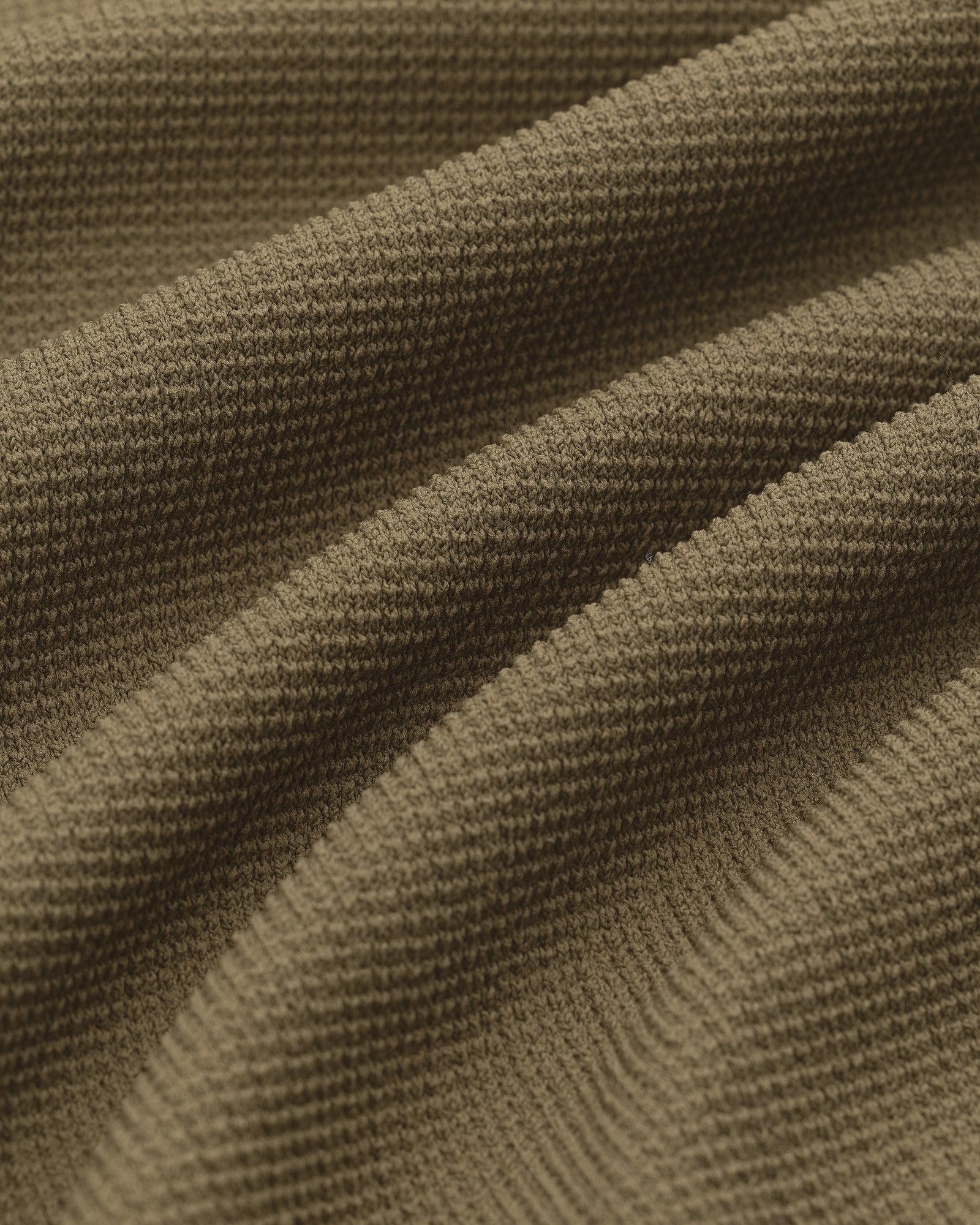 Close-up of textured, olive-green Knit Polo fabric with ridged knit pattern and soft, wavy folds.