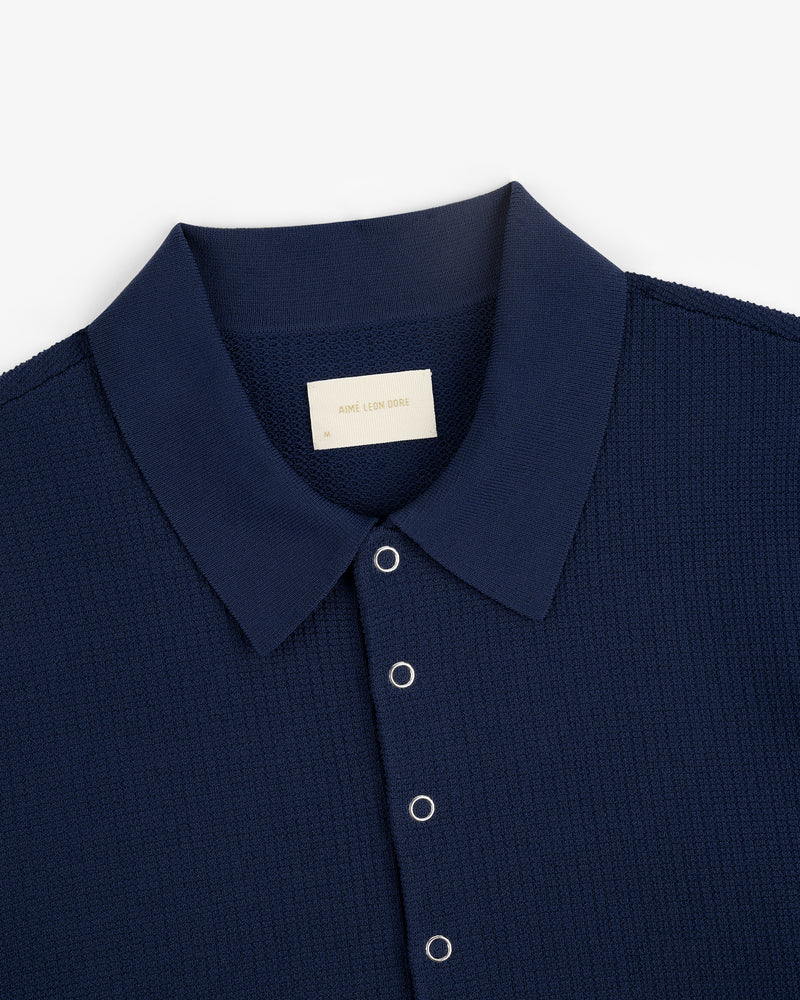 Navy blue Knit Polo with silver snap buttons and a visible Aimé Leon Dore label on the inside collar.