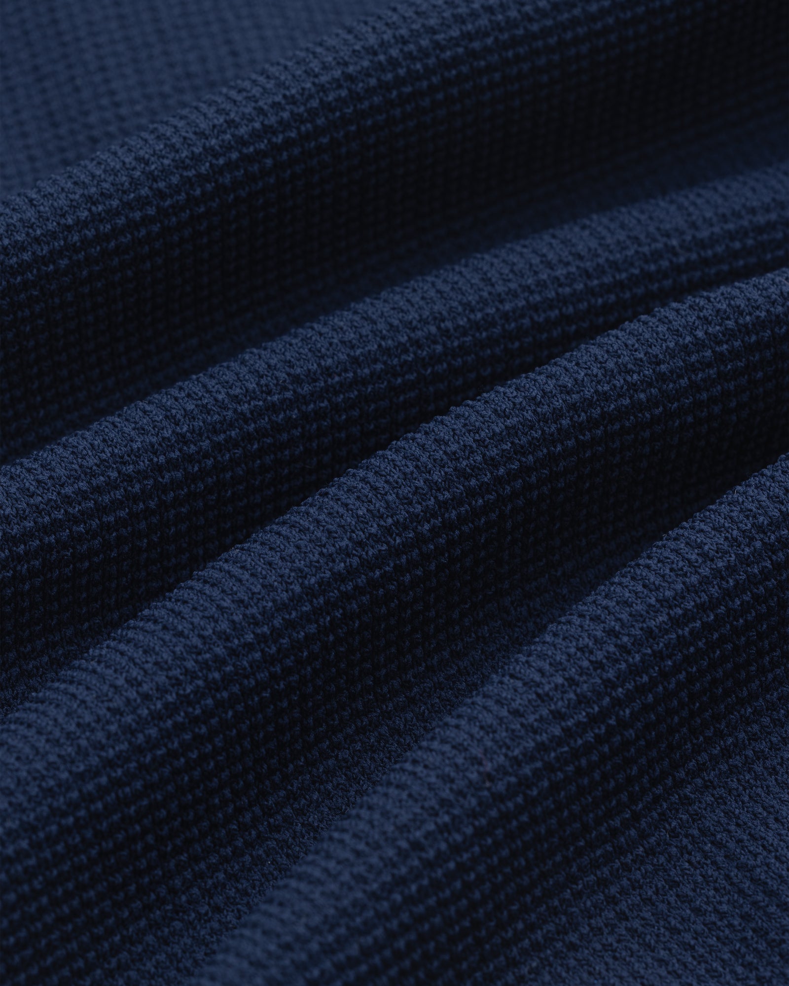 Close-up of the Knit Polo in dark blue, featuring a textured waffle weave and softly draped folds.