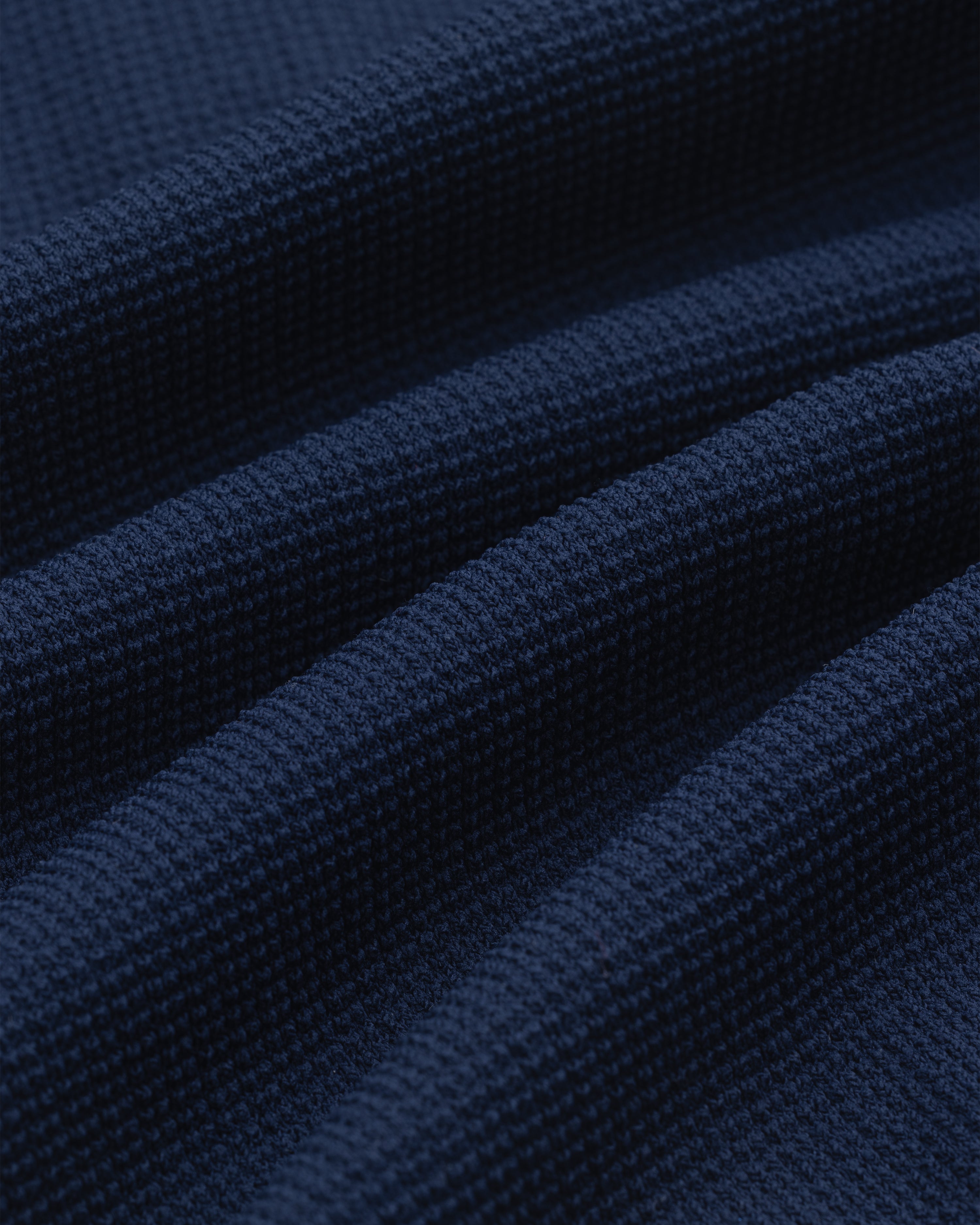 Close-up of the Knit Polo in dark blue, featuring a textured waffle weave and softly draped folds.