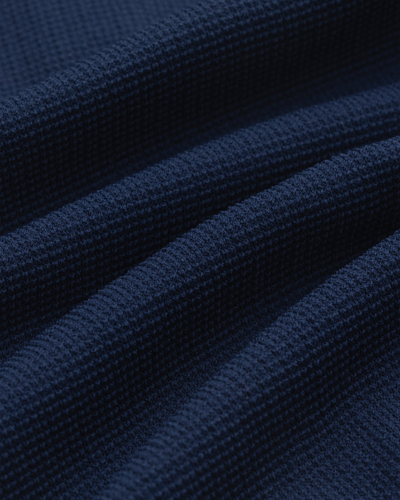 Close-up of the Knit Polo in dark blue, featuring a textured waffle weave and softly draped folds.