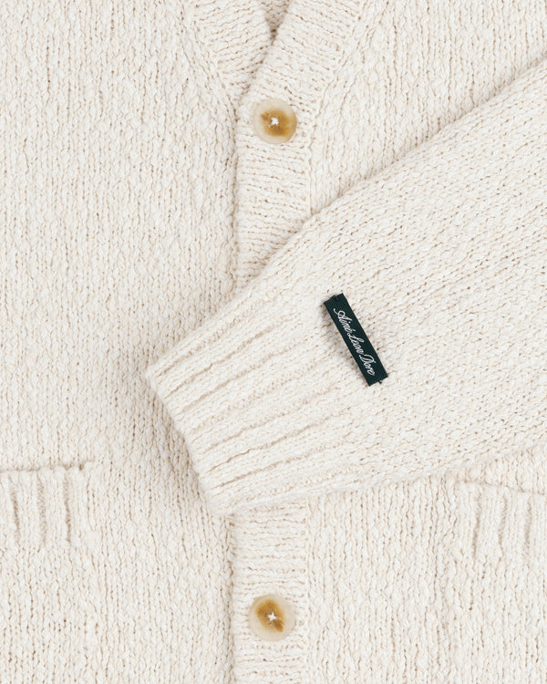 Close-up of the Cotton Slub Cardigan in cream, featuring tan buttons and a small black sleeve label.