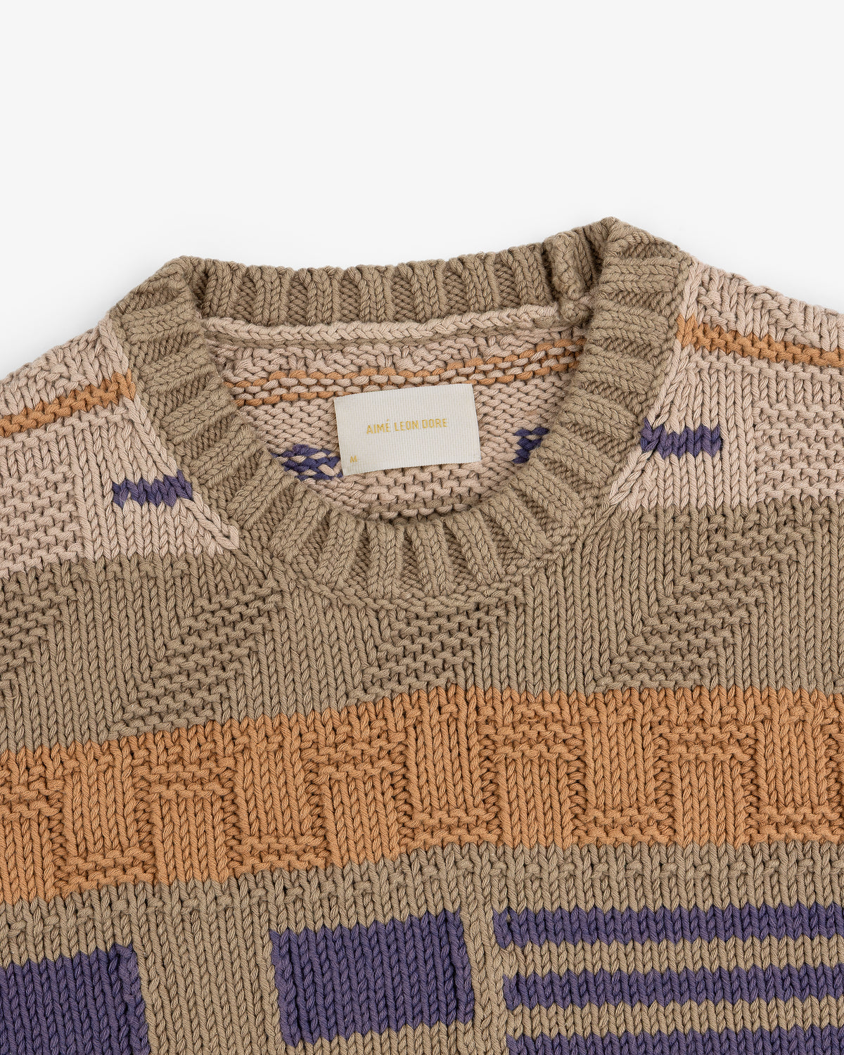 The Simaía Crewneck Sweater features beige, tan, orange, and purple geometric patterns with a ribbed crewneck collar.