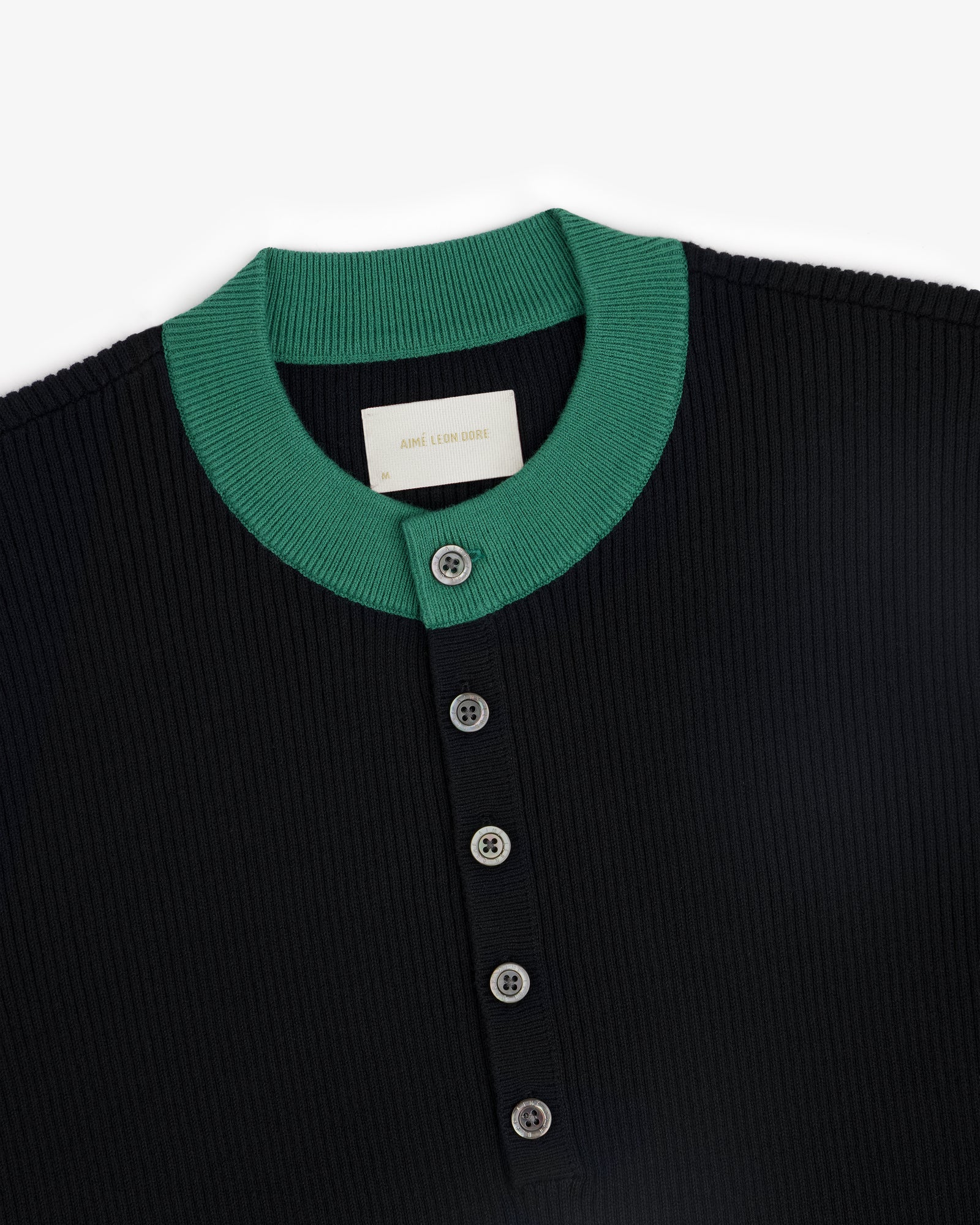 Close-up of the Sport Knit Henley, a ribbed black shirt with a green collar and four front buttons.