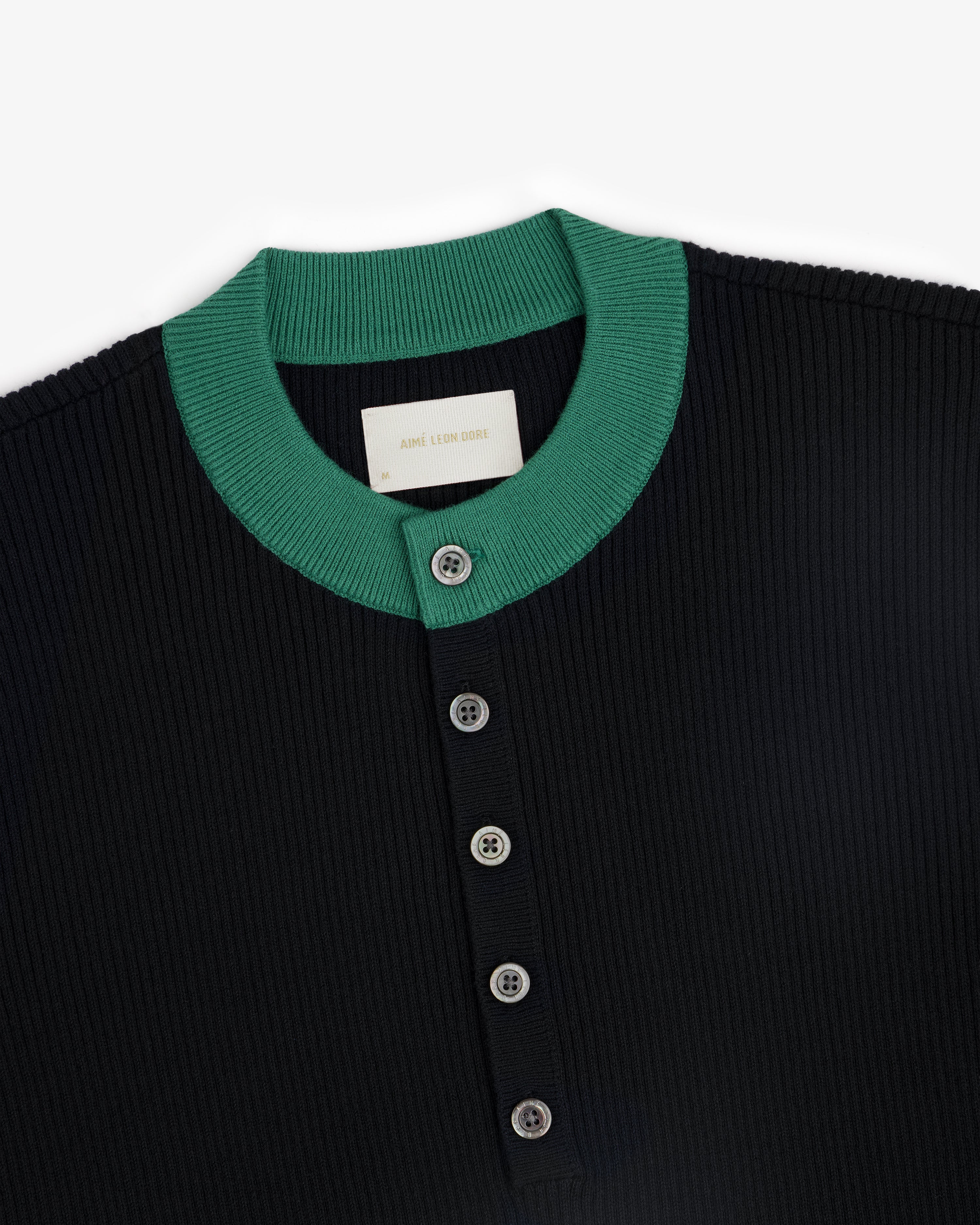Close-up of the Sport Knit Henley, a ribbed black shirt with a green collar and four front buttons.