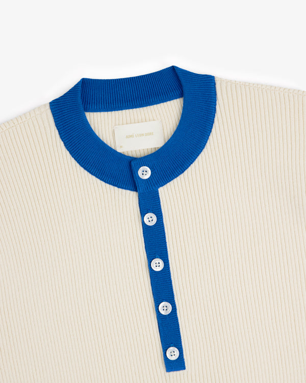 Sport Knit Henley—cream ribbed shirt with bright blue collar, button placket, and four white buttons.