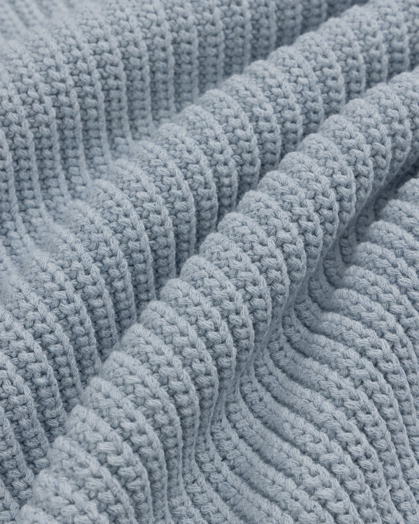 Close-up of the Knit Denim Crewneck Sweater featuring soft, light blue knit fabric with ribbed texture and wavy folds.
