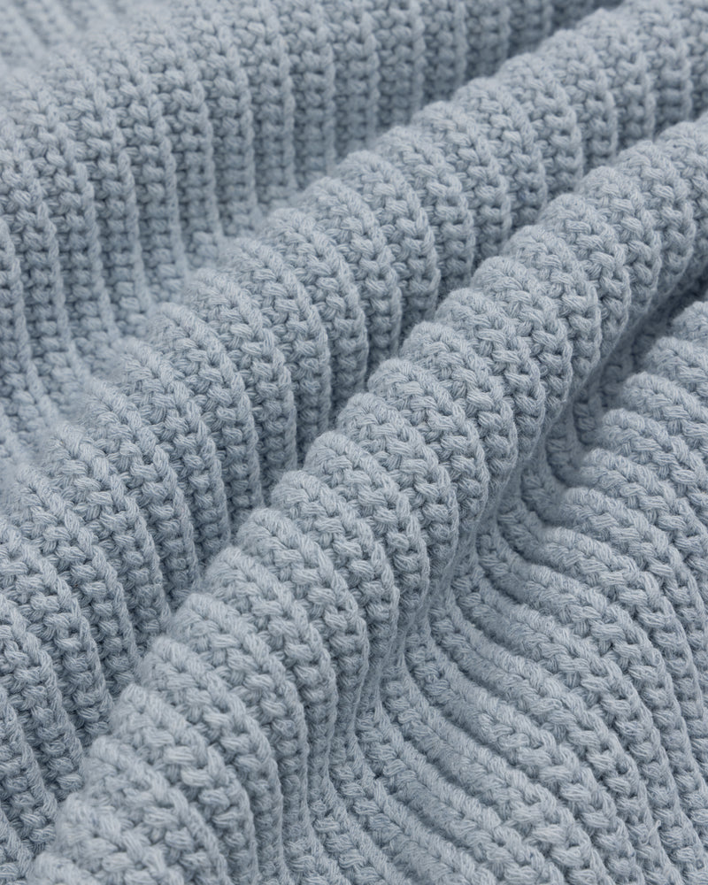 Close-up of the Knit Denim Crewneck Sweater featuring soft, light blue knit fabric with ribbed texture and wavy folds.