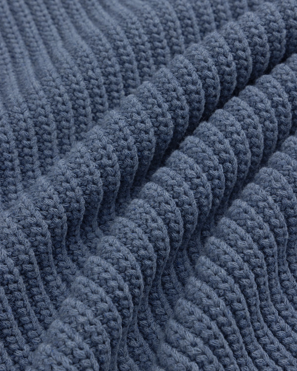 Close-up of Knit Denim Crewneck Sweater's blue ribbed knit fabric, highlighting its textured rows and folds.