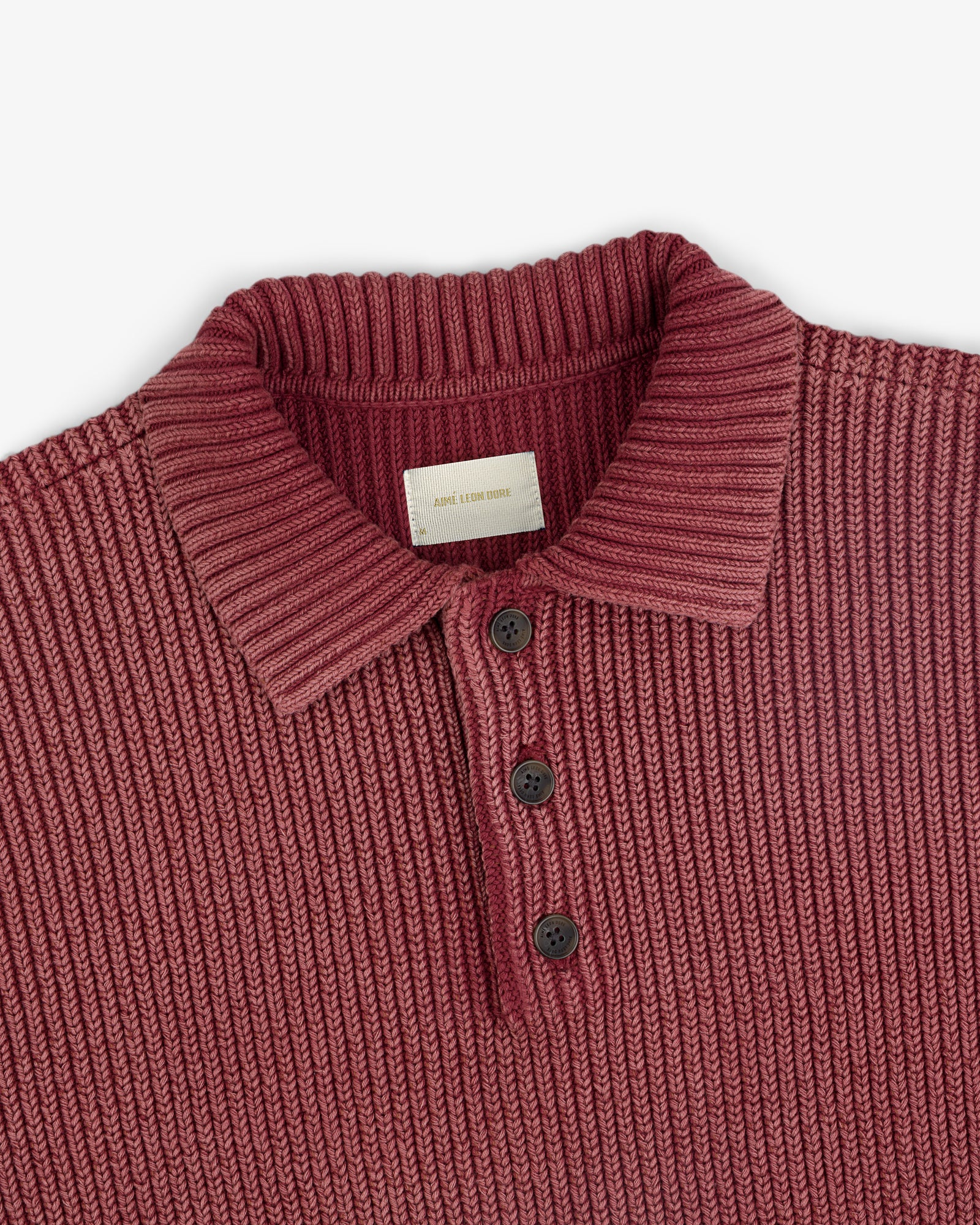 The Stone Washed Knit Polo is ribbed, maroon, with a collar and three black buttons down the front.
