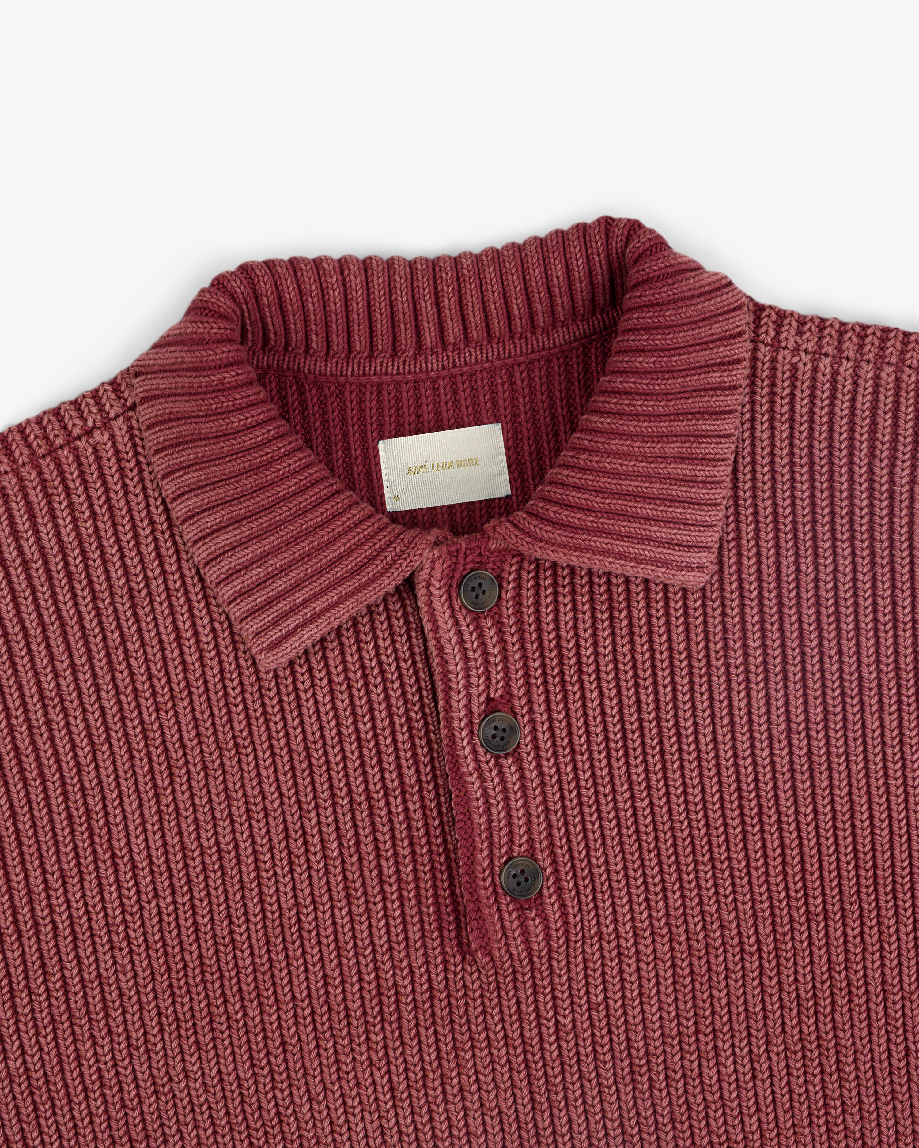 The Stone Washed Knit Polo is ribbed, maroon, with a collar and three black buttons down the front.
