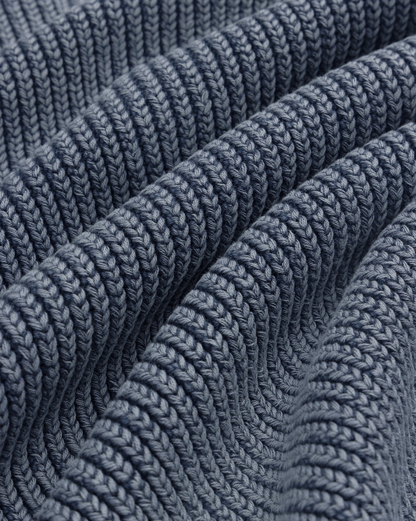 Close-up of thick, textured rows and soft folds on blue Stone Washed Knit Polo fabric.
