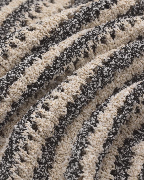 Close-up of Bouclé Open Knit Crewneck Sweater with ribbed, textured fabric and beige-black stripes.