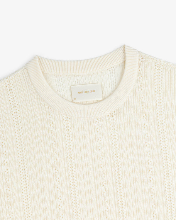 Ivory Merino Wool Eyelet Tee with a ribbed crew neckline and a beige “AIME LEON DORE” label inside the collar.