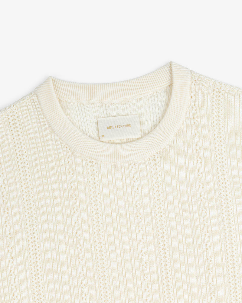 Ivory Merino Wool Eyelet Tee with a ribbed crew neckline and a beige “AIME LEON DORE” label inside the collar.