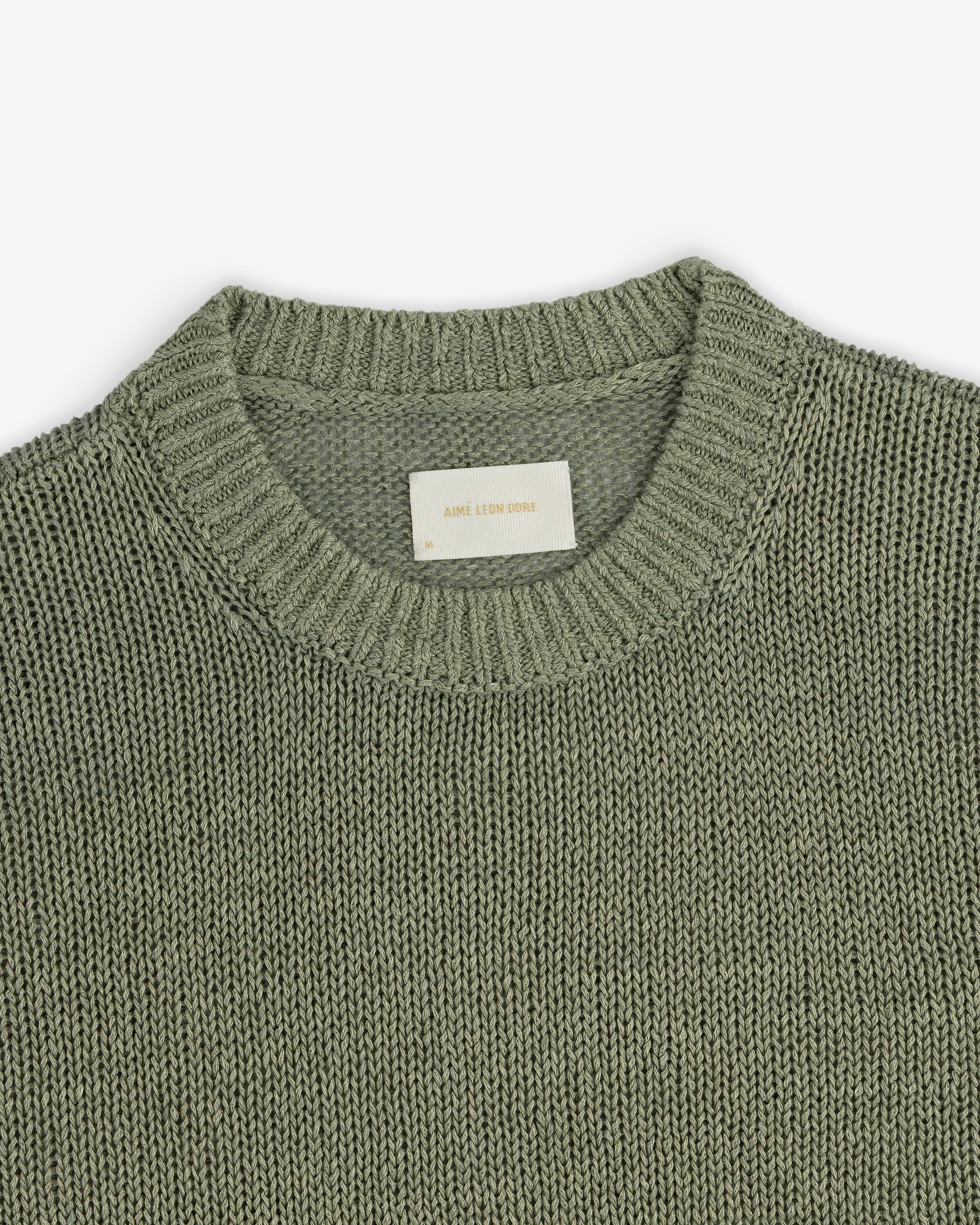 A close-up of the Linen Knit Crewneck Sweater in sage green, featuring a ribbed neckline and white inner label.