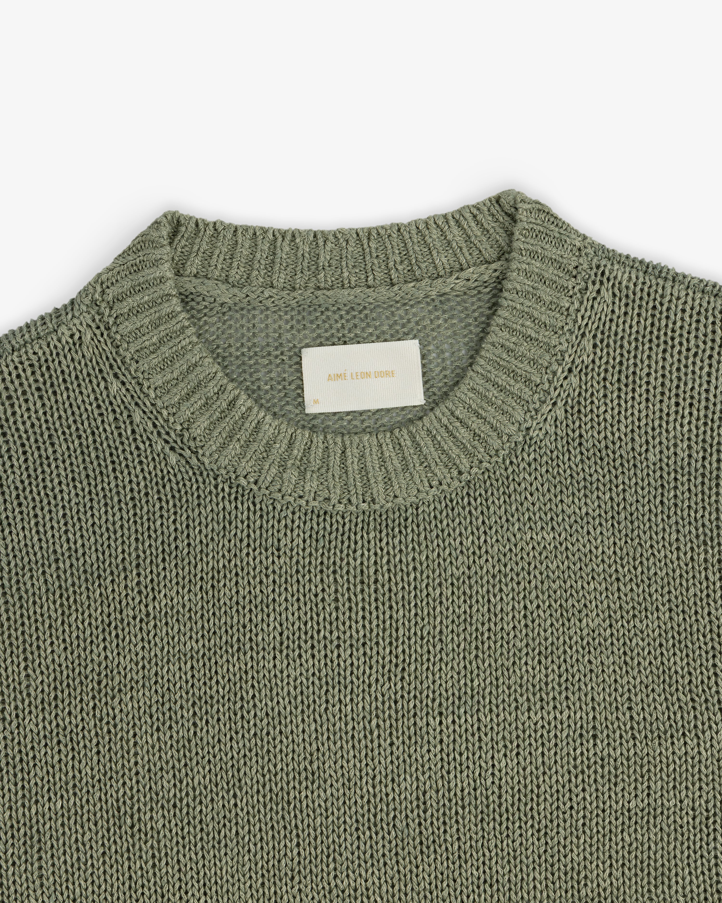 A close-up of the Linen Knit Crewneck Sweater in sage green, featuring a ribbed neckline and white inner label.