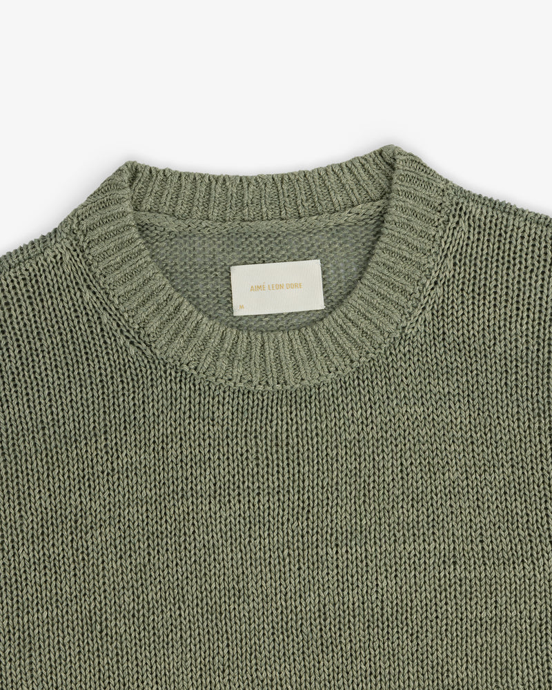 A close-up of the Linen Knit Crewneck Sweater in sage green, featuring a ribbed neckline and white inner label.