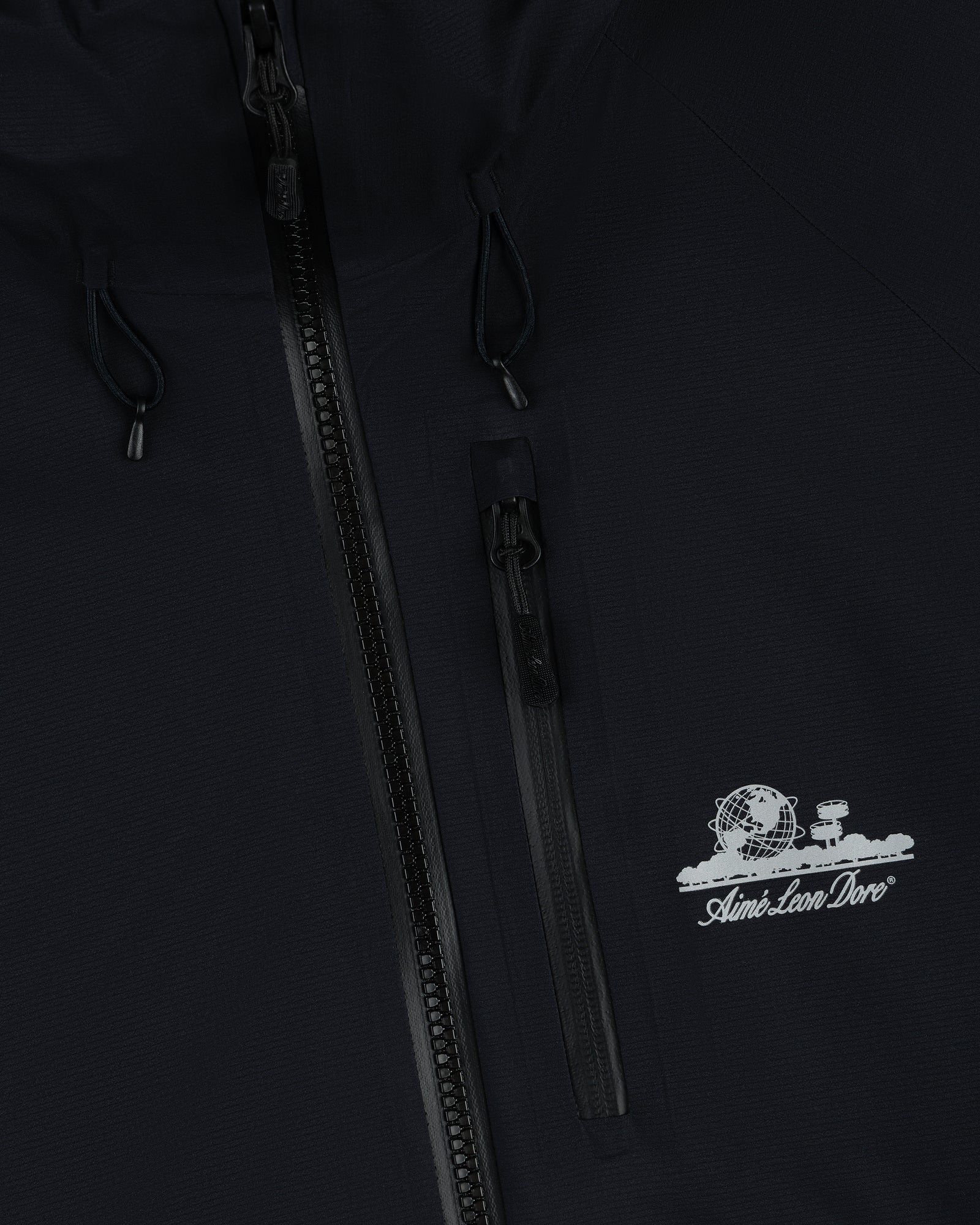 Close-up of black Lightweight GORE-TEX Shell Jacket with zipper and white Aimé Leon Dore globe and tree logo.