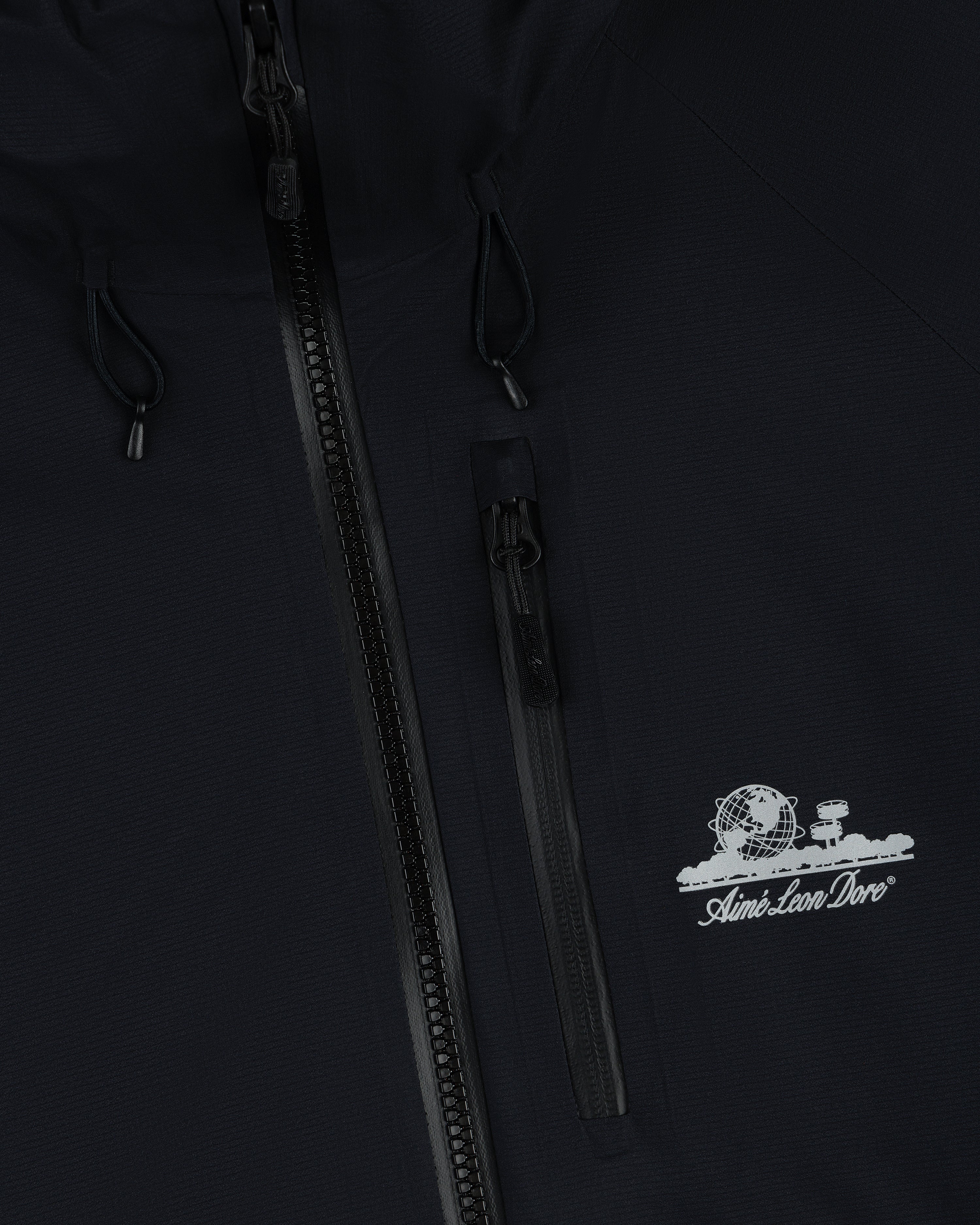 Close-up of black Lightweight GORE-TEX Shell Jacket with zipper and white Aimé Leon Dore globe and tree logo.
