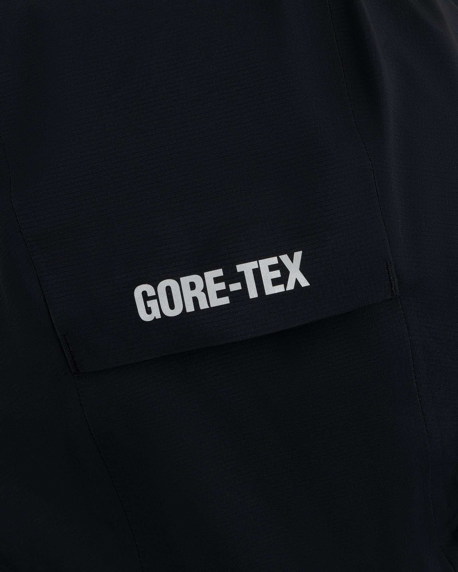 Close-up of a Lightweight GORE-TEX Shell Jacket in black, featuring a white GORE-TEX logo on the pocket flap.
