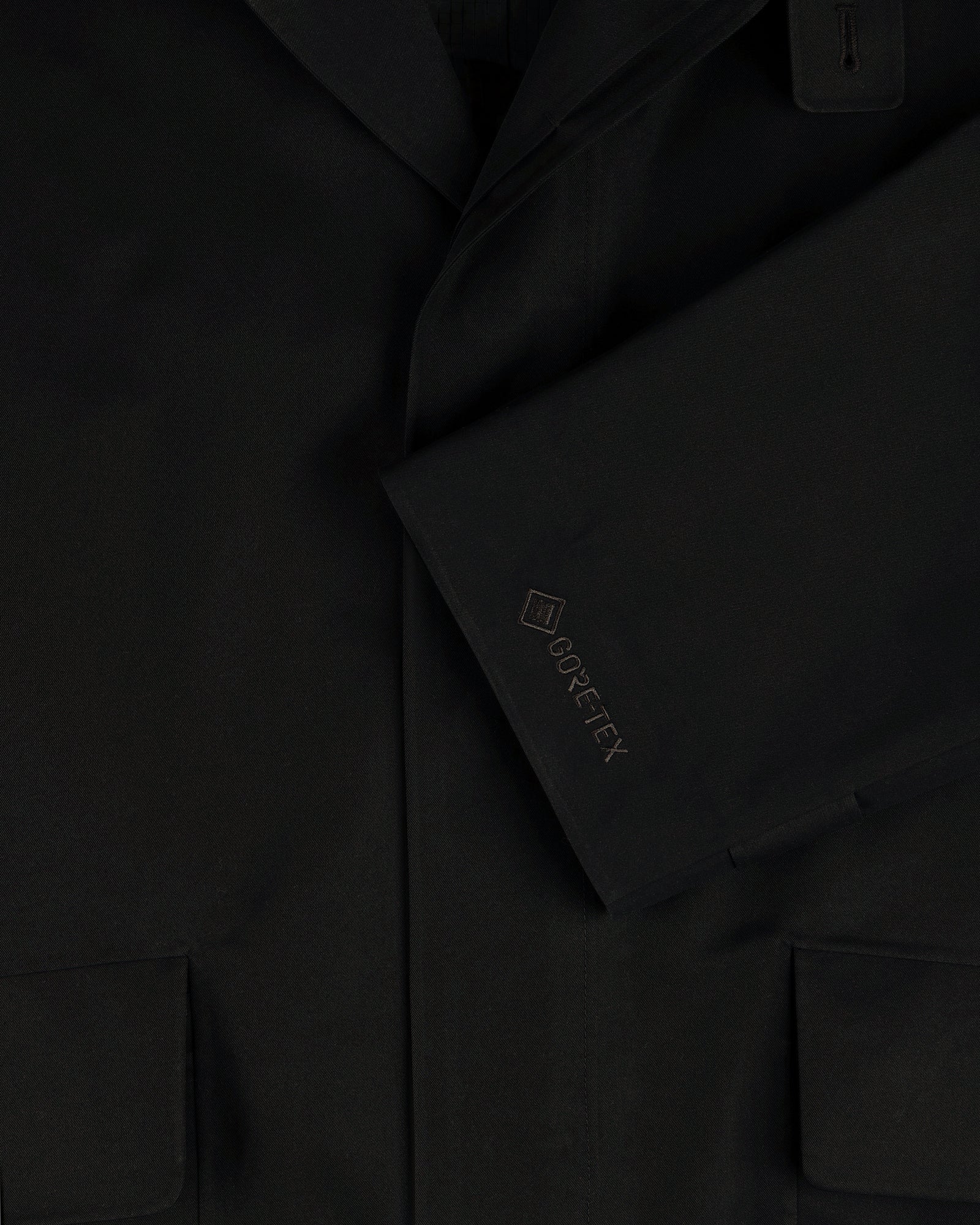 Close-up of the GORE-TEX Balmacaan Coat’s black sleeve with GORE-TEX embroidery and two front pockets.