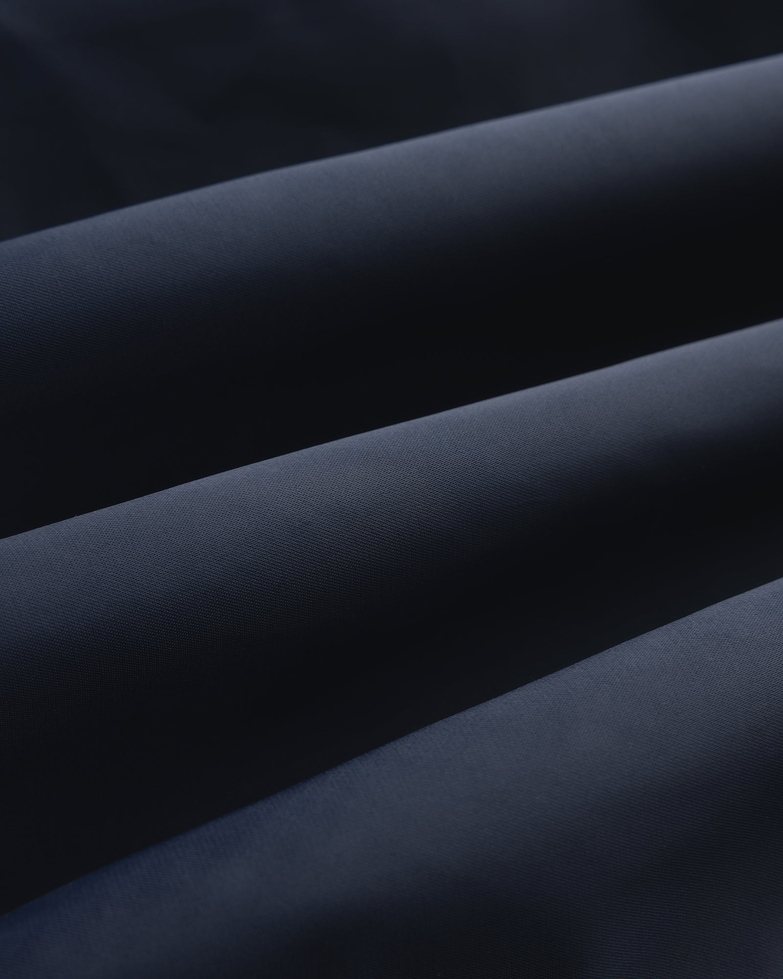 Close-up of folded Overlay Logo Satin Varsity Jacket in dark blue with a soft, smooth texture and gentle shadows.