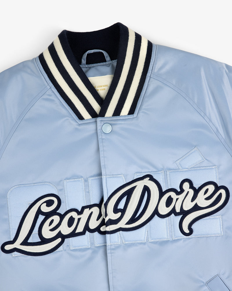 Light blue Overlay Logo Satin Varsity Jacket with navy-white striped collar and cursive Leon Dore embroidery on front.