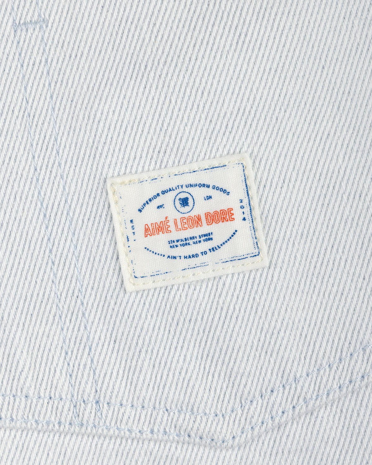 White Denim Barn Jacket with a small rectangular patch reading AIMÉ LEON DORE in red and blue text.