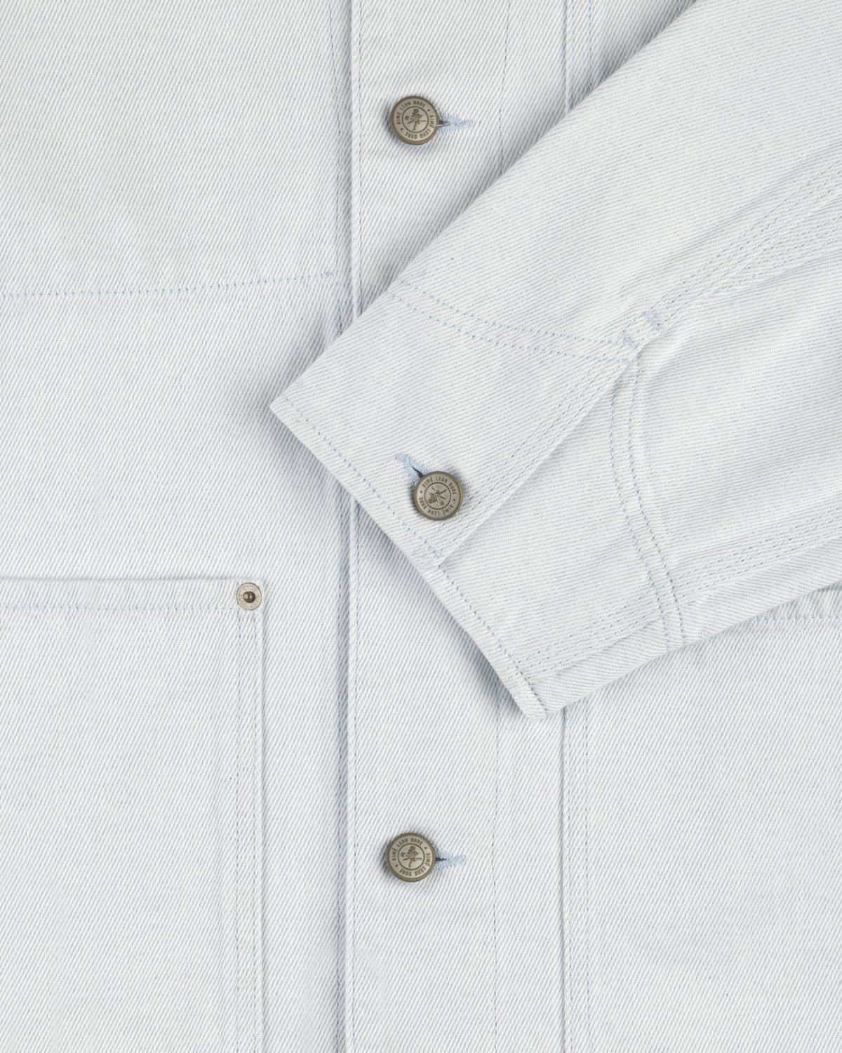 Close-up of the Denim Barn Jacket in light blue, showing metal buttons, front pocket, and folded sleeve.