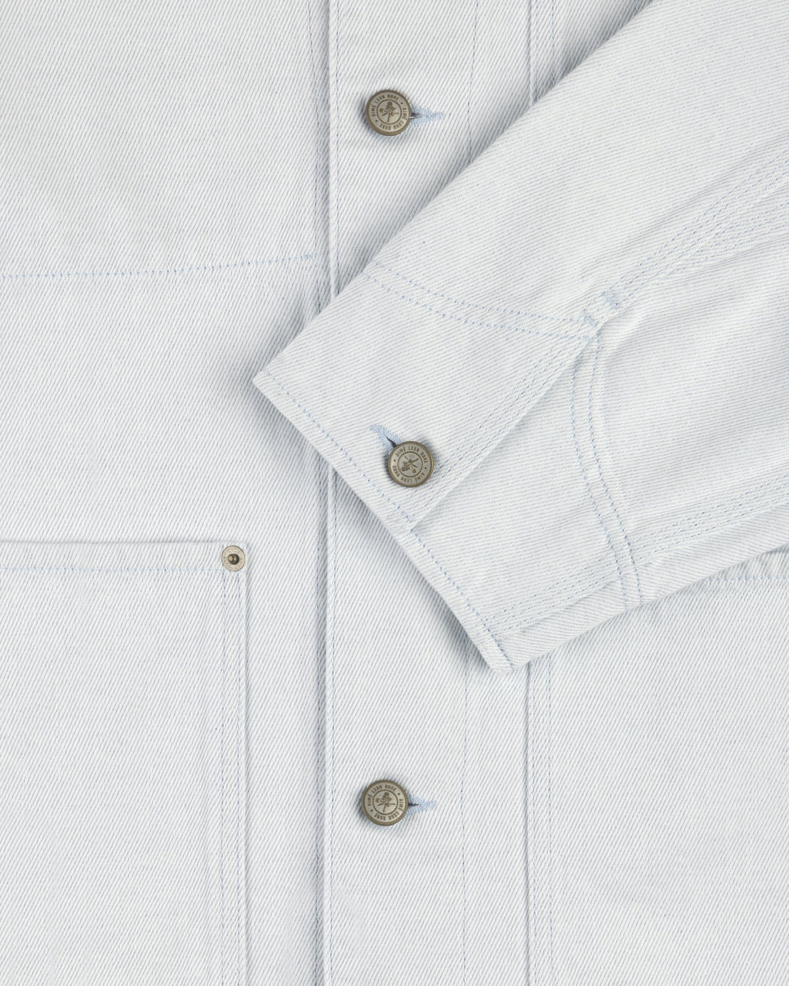 Close-up of the Denim Barn Jacket in light blue, showing metal buttons, front pocket, and folded sleeve.