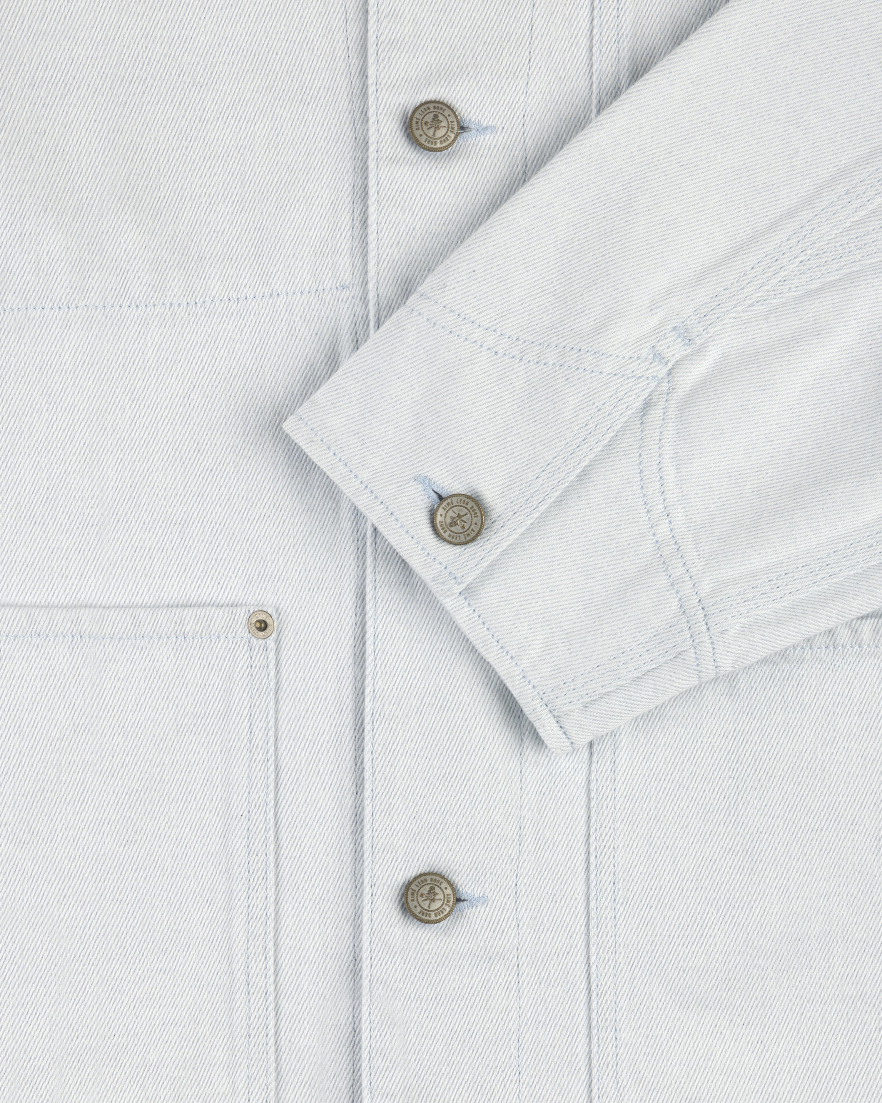 Close-up of the Denim Barn Jacket in light blue, showing metal buttons, front pocket, and folded sleeve.