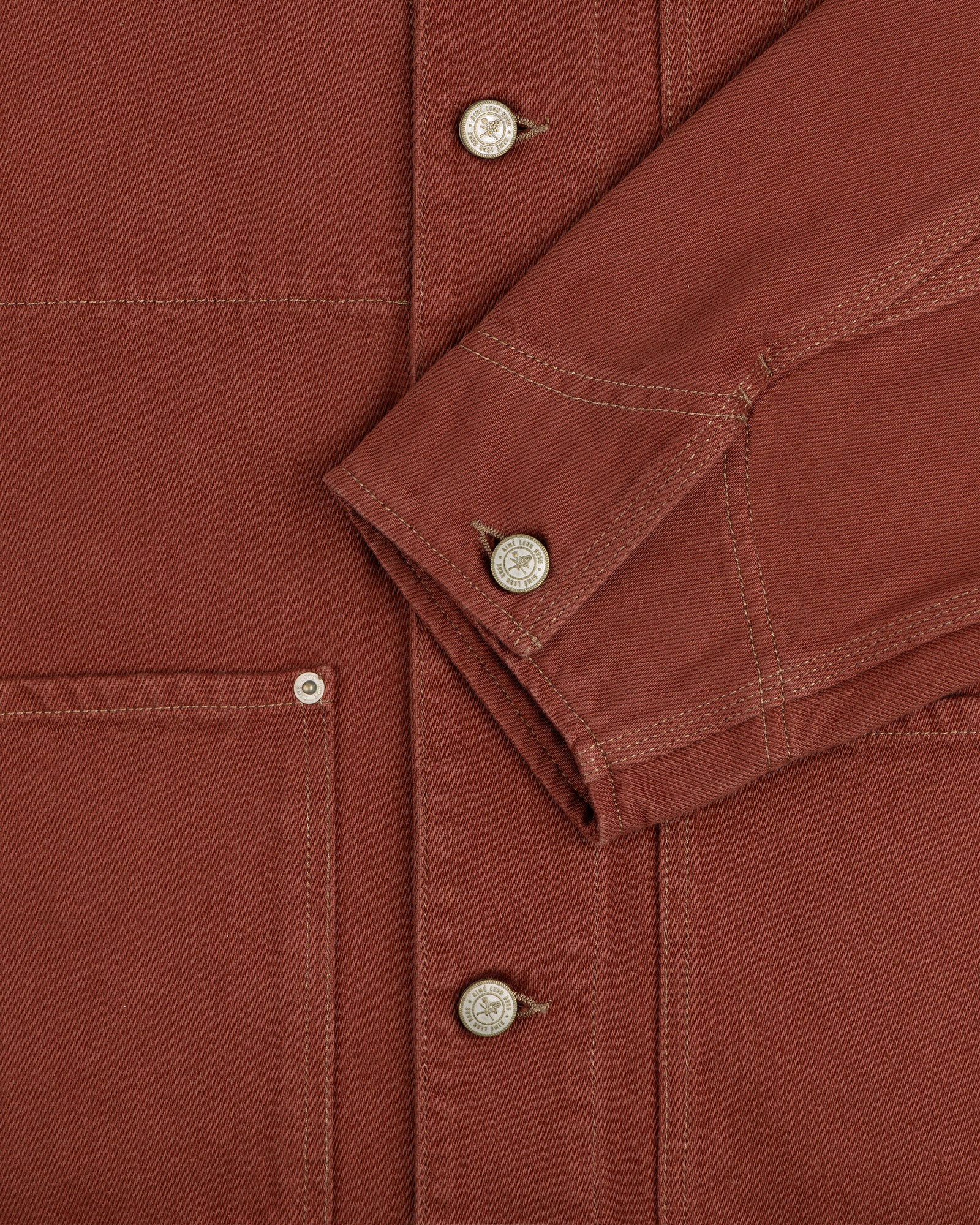 Close-up of the Denim Barn Jacket in rust, highlighting buttons, a pocket, and a folded sleeve with visible stitching.