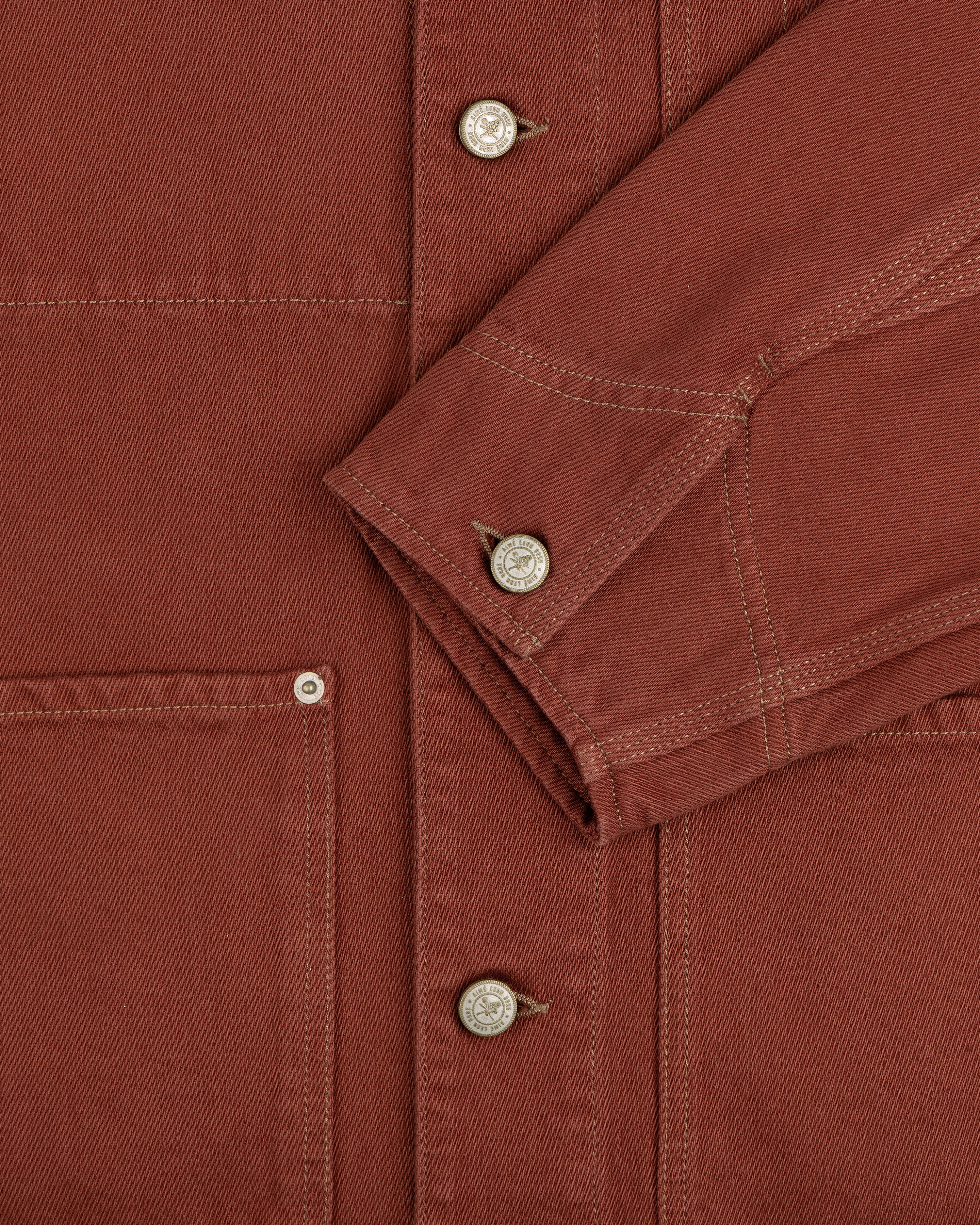 Close-up of the Denim Barn Jacket in rust, highlighting buttons, a pocket, and a folded sleeve with visible stitching.