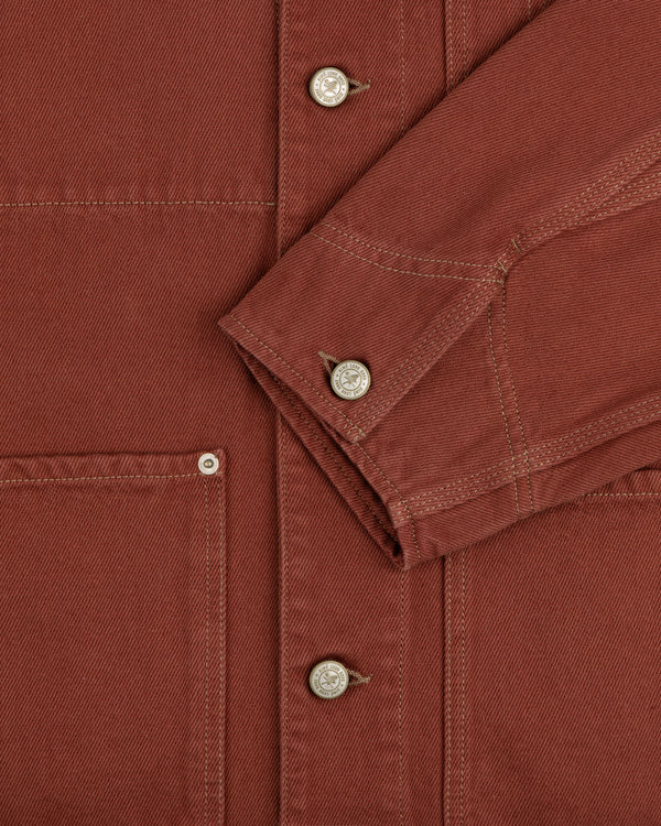 Close-up of the Denim Barn Jacket in rust, highlighting buttons, a pocket, and a folded sleeve with visible stitching.
