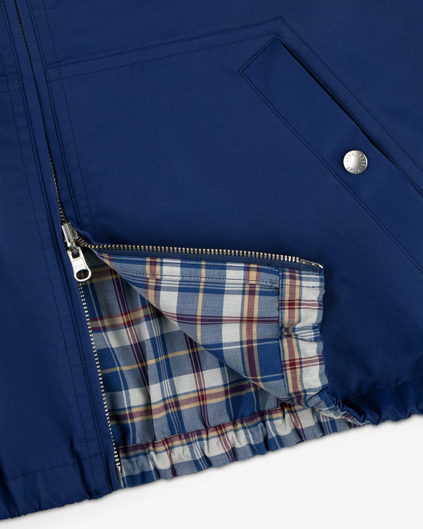 Close-up of Reversible Madras Windbreaker in blue, zipper open to reveal plaid lining and snap-button pocket.
