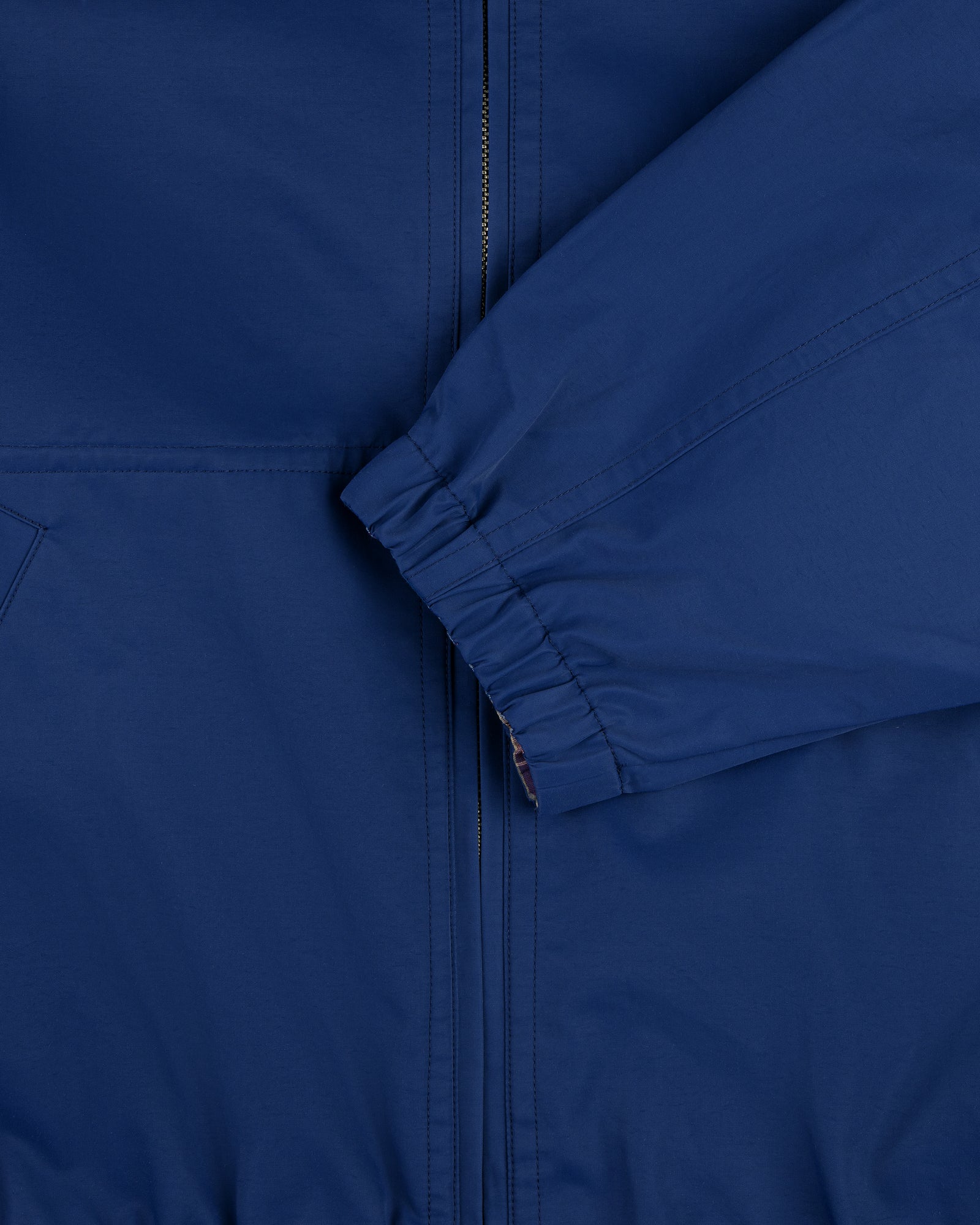 Close-up of the Reversible Madras Windbreaker in blue with a visible zipper, pocket seam, and folded sleeve.