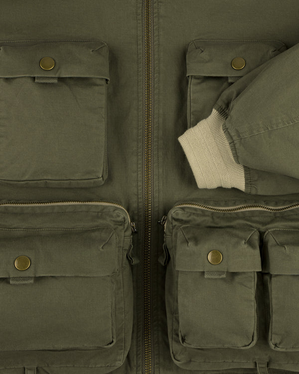 Close-up of the Safari Utility Bomber in olive green, featuring front pockets and a beige ribbed cuff on one sleeve.