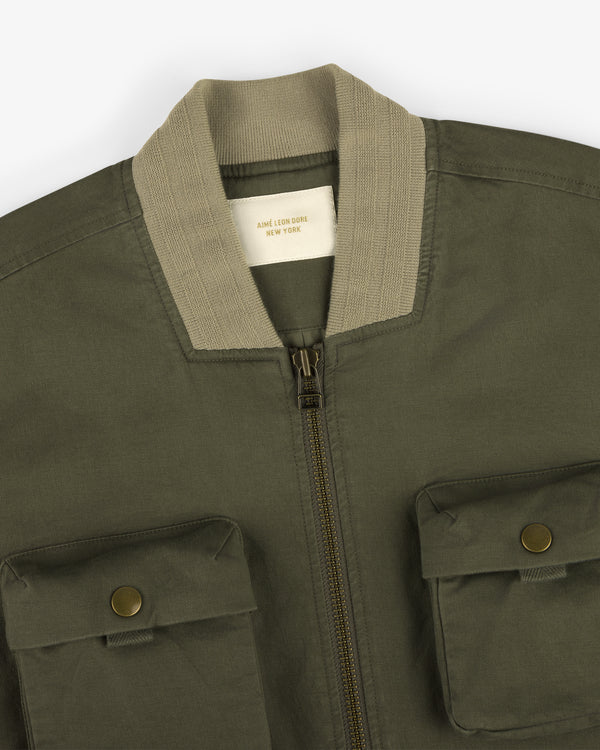 Safari Utility Bomber in olive green with front zipper, two flap pockets, and a beige ribbed collar.