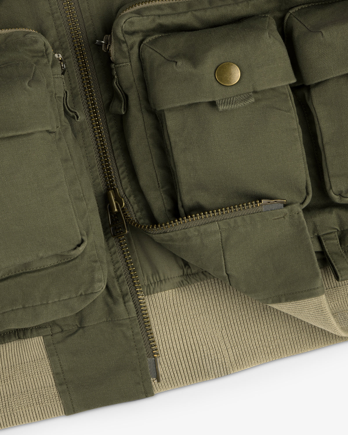 Close-up of the Safari Utility Bomber in olive green with front pockets, zippers, and a beige ribbed hem.