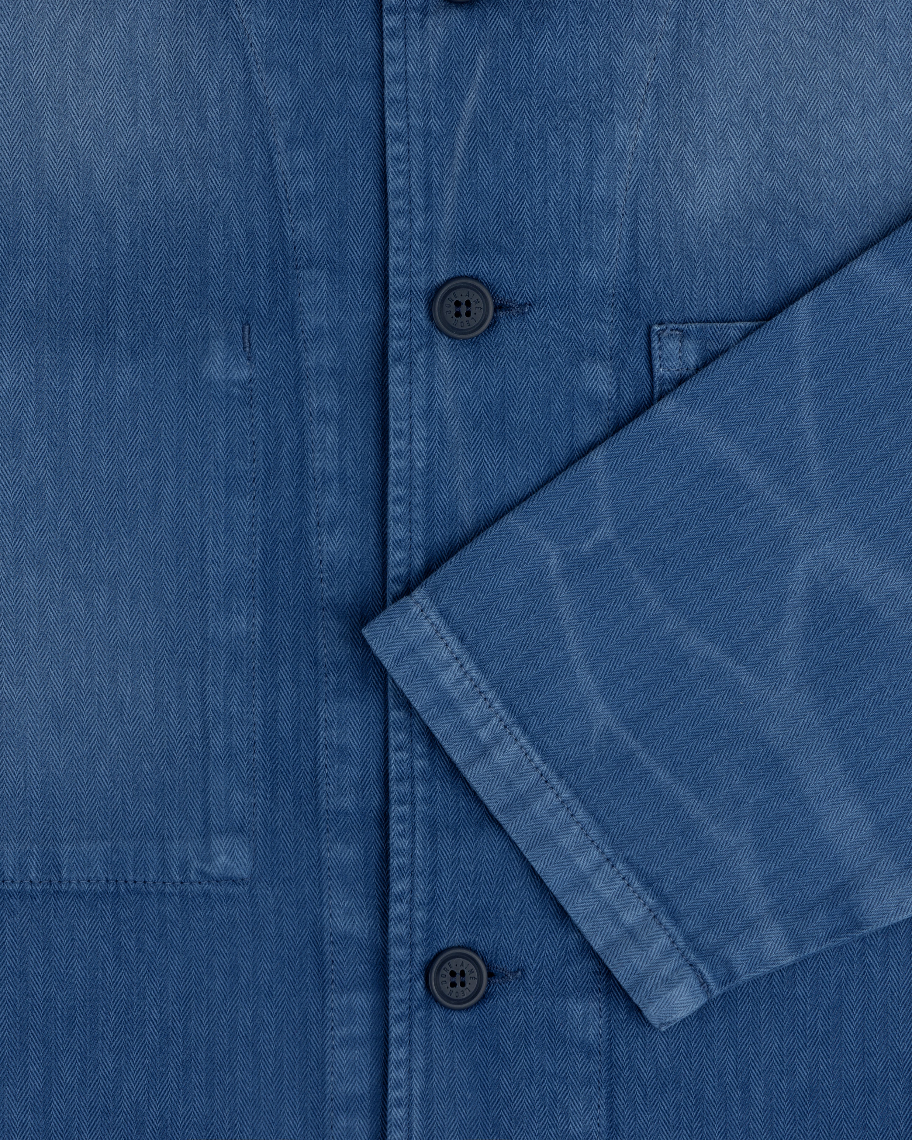 Close-up of the Sun Faded Chore Jacket, a blue button-up with a chest pocket and sleeve crossing the front.